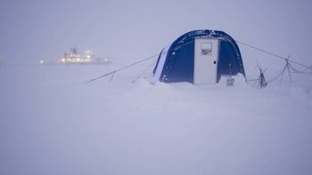 Ein blaues Zelt steht im Vordergrund auf einer Eisscholle. Im Hintergrund sieht man das beleuchtete Forschungsschiff.