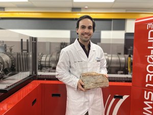 Wissenschaftler im weißen Kittel mit einem schweren Stein in der Hand