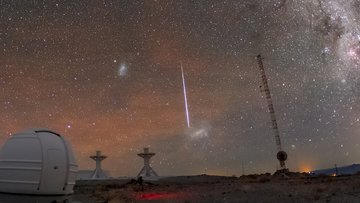 Sternschnuppe mit langem, hellem Schweif am Nachthimmel über mehreren Teleskopanlagen; deutlich sichtbar auch die Milchstraße