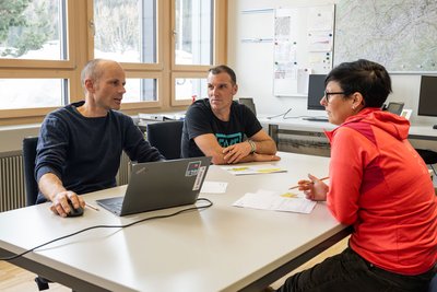 Drei Personen sitzen an einem Tisch und unterhalten sich.