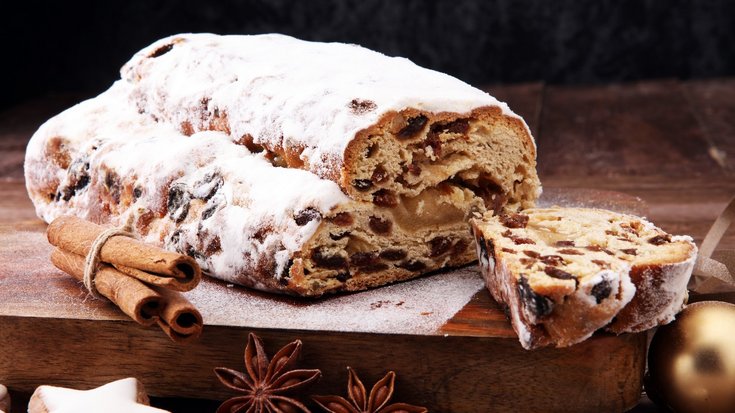 Das Foto zeigt einen aufgeschnittenen Christstollen. Daneben liegen einige Zimtstangen und Zimtsterne.