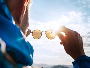 Das Foto zeigt einen Mann, der eine Sonnenbrille in den Händen hält.