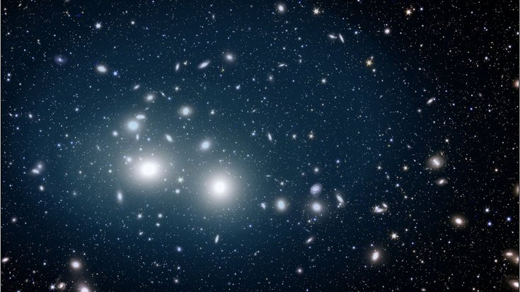 Viele Galaxien und Leuchtpunkte auf dunklem Hintergrund. Mittig links häufen sich Galaxien und zwei von ihnen leuchten besonders stark im Vordergrund.